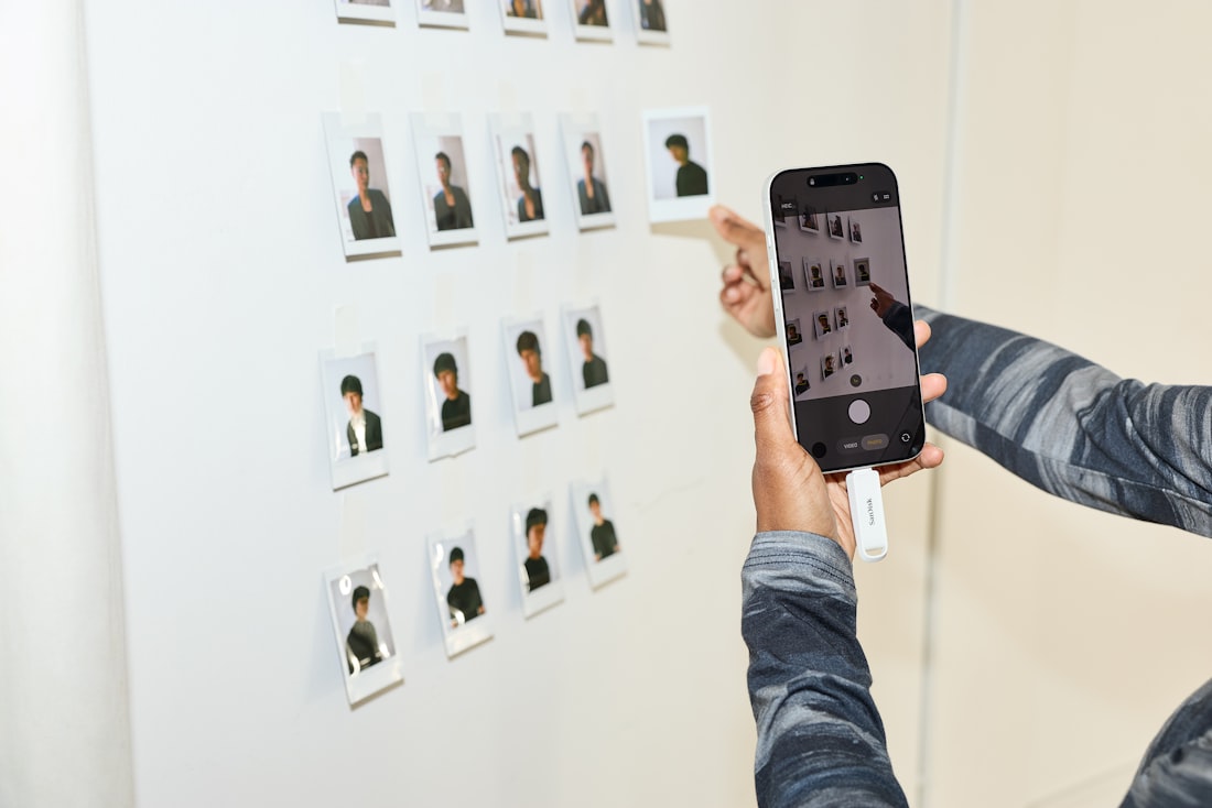 Person photographs small pictures on a white wall with phone.